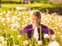 Mädchen auf Wiese mit Pusteblumen und Allergie